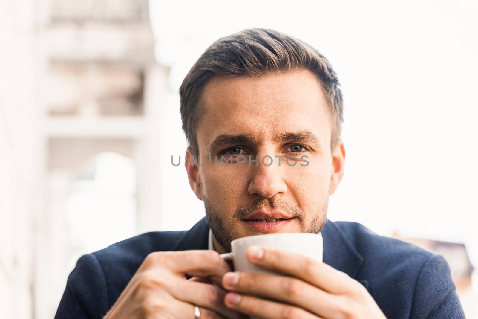Man like coffee. Handsome man with cup of coffee in cafe. Morning lifestyle of male. Man is sitting on the summer terrace in cafe, drinking coffee and smiling. by Rabizo