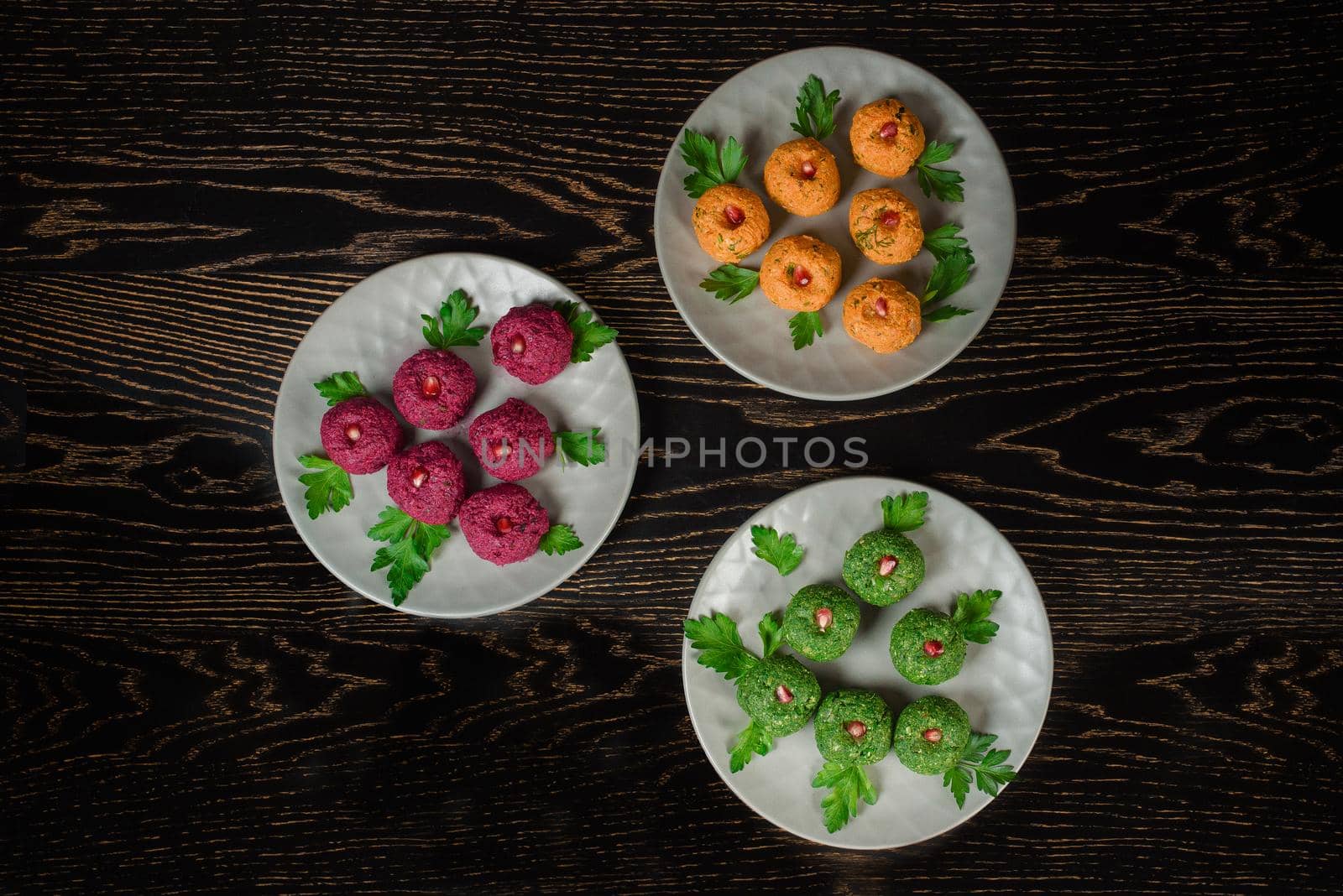 Assortment of pkhali from beets, spinach, carrots, garnished with parsley and pomegranate. Georgian appetizer on a gray plate on a dark wooden table. Top view by Rabizo