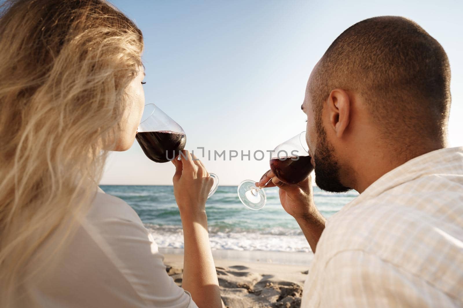 Portrait of a young couple sitting on the beach and drinking wine, close up