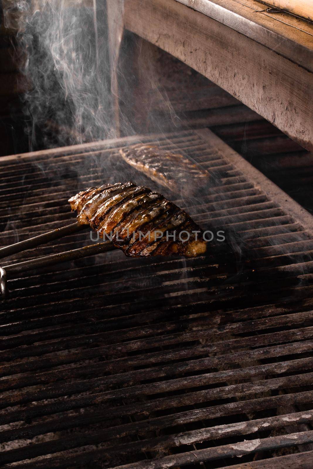 Grilling chicken fillets with metal tongs. The cook prepares a barbecue dish by Rabizo