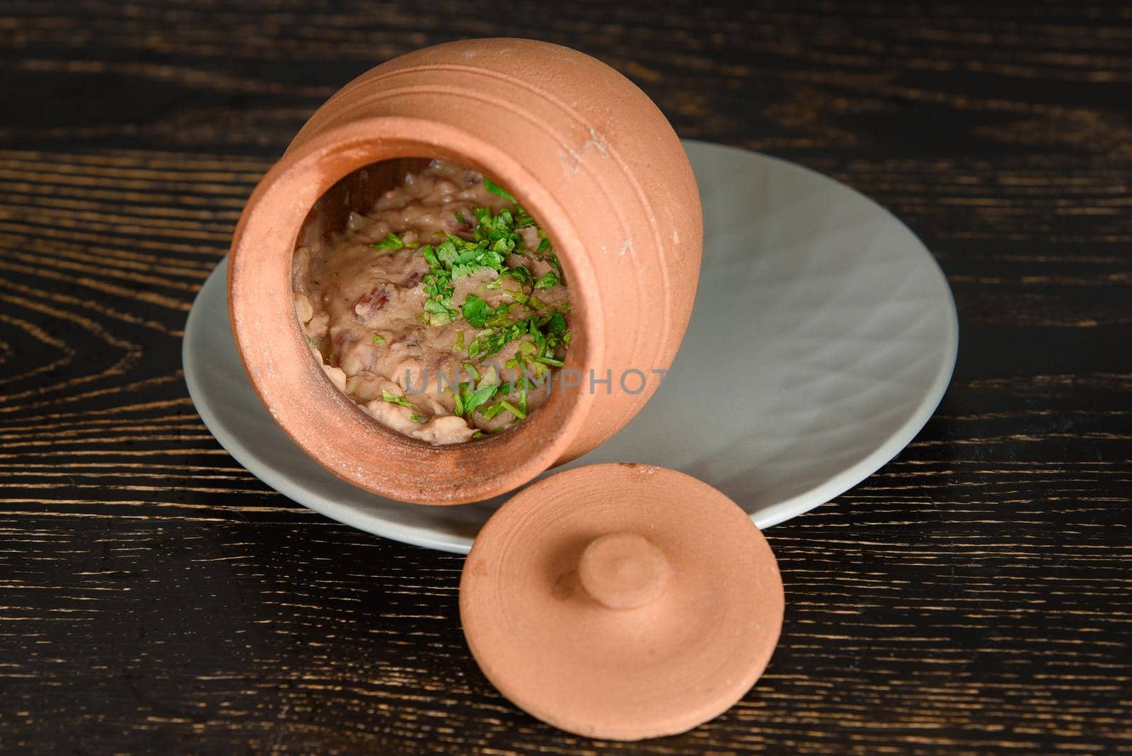 A dish baked in a clay pot decorated with herbs on a dark wooden table.