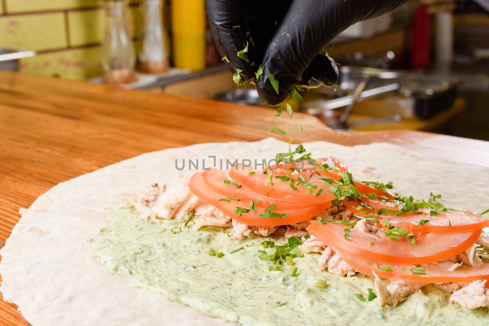 Burrito cooking process. Cook adds greens to tomato and meat on pita with sauce. Mexican dish by Rabizo