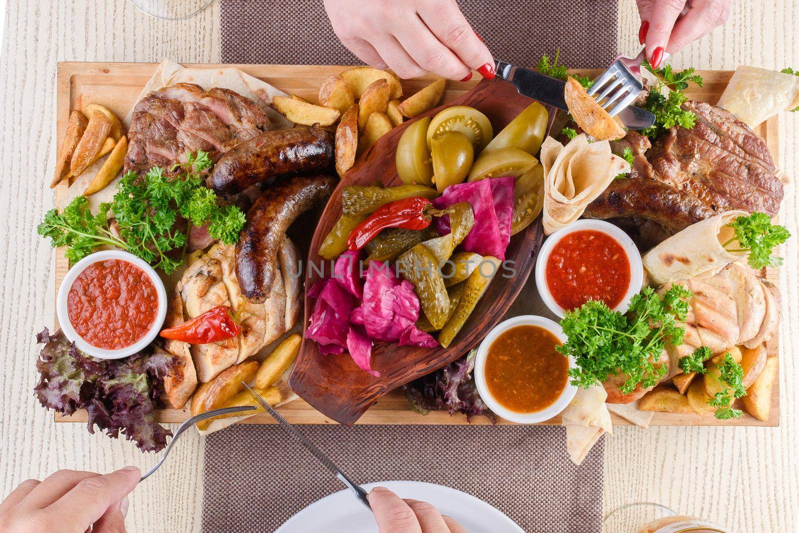 Assortment of fried meat, potatoes, sausages, pickles, tomatoes, peppers, herbs, lavash on a wooden tray on the table. Top view. by Rabizo