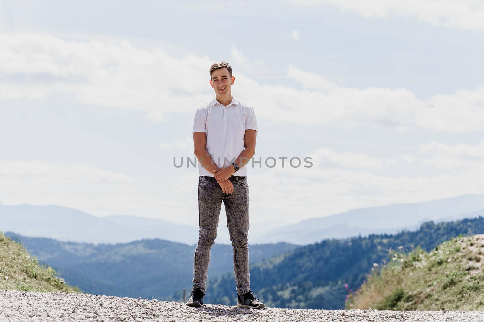 Handsome man is walking on the green hills background. Advert for travel agency. Tourism. Travelling in the mountains.