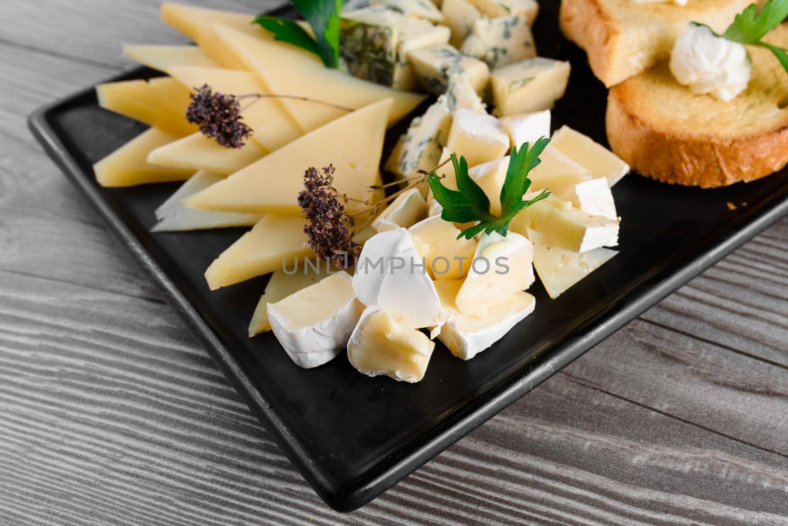 Cheese food board with delicous cheeses, walnuts. Parmesan, jam, dorblu on the black plate. Food appetizer from restaurant. by Rabizo