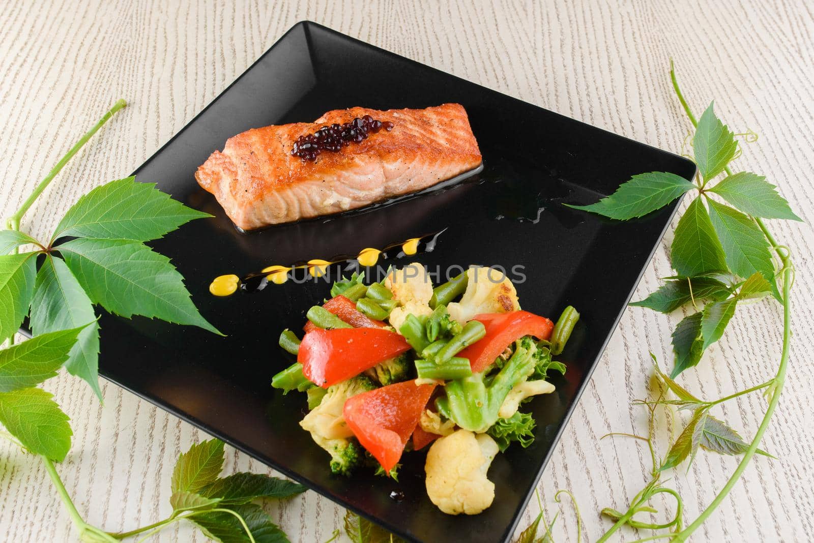 Salmon fillet with fried vegetables on square black plates on a white wooden table. by Rabizo