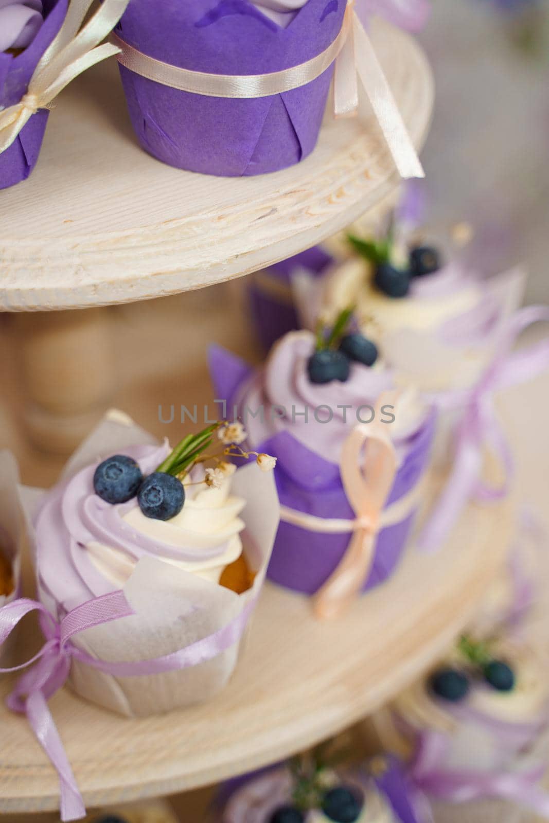 Vanilla cupcakes with lavender cream. Thematic muffins. Cupcakes with cream in a paper tulip form, decorated with blueberries, rosemary, flowers, tied with a ribbon.