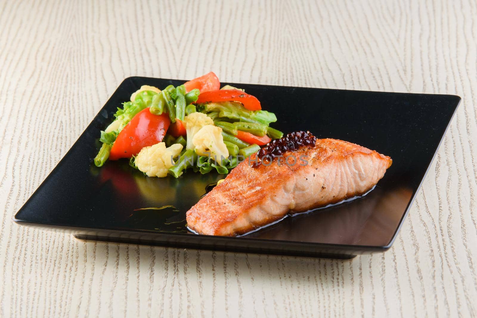 Salmon fillet with fried vegetables on square black plates on a white wooden table. by Rabizo