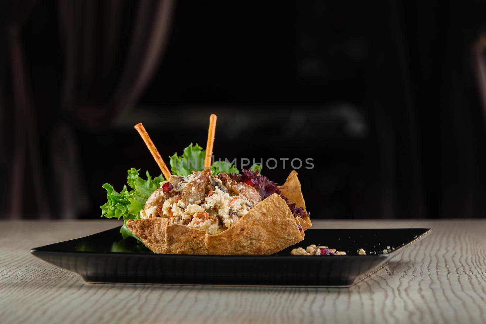 Pilaf in the form of fried pita bread, garnished with bread sticks and lettuce on a black square plate on a white wooden table by Rabizo