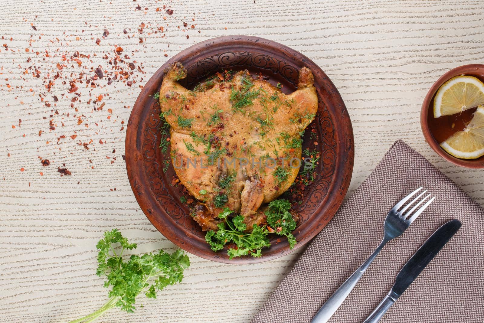 Tobacco chicken decorated with herbs on a clay plate on a white wooden table. Top view
