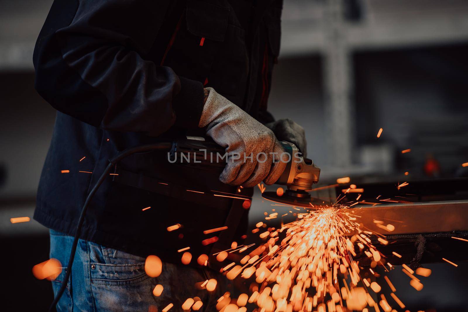 Heavy Industry Engineering Factory Interior with Industrial Worker Using Angle Grinder and Cutting a Metal Tube. Contractor in Safety Uniform and Hard Hat Manufacturing Metal Structures. High-quality photo