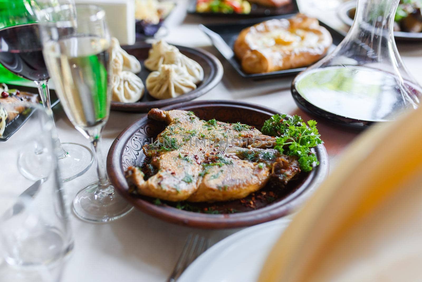 Assortment of dishes chicken tabaka, khachapuri, khinkali against the background of a bowl of wine, glasses of champagne. Table setting