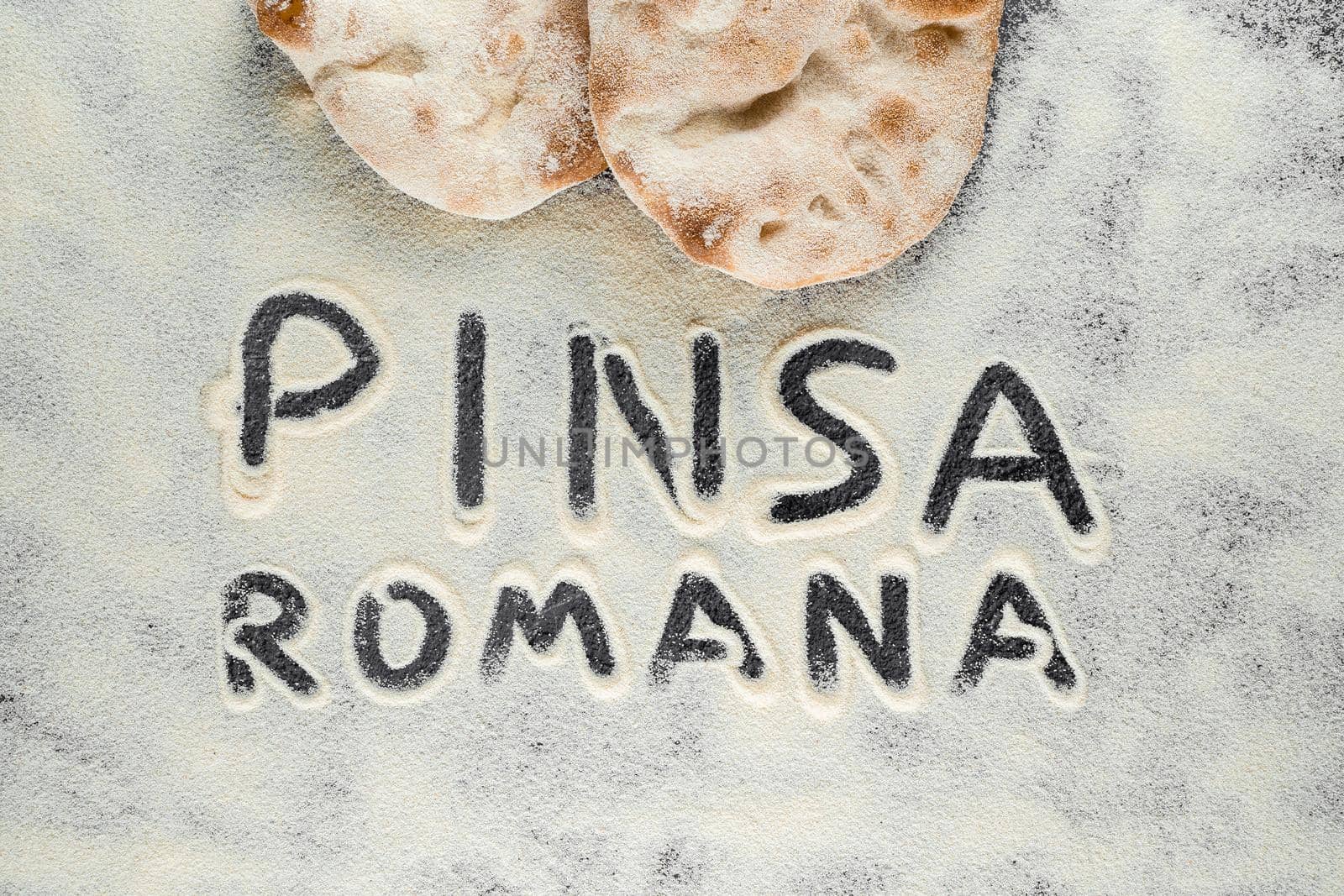Dough and flour with text pinsa romana on black background. Scrocchiarella gourmet italian cuisine. Traditional dish in italy. by Rabizo