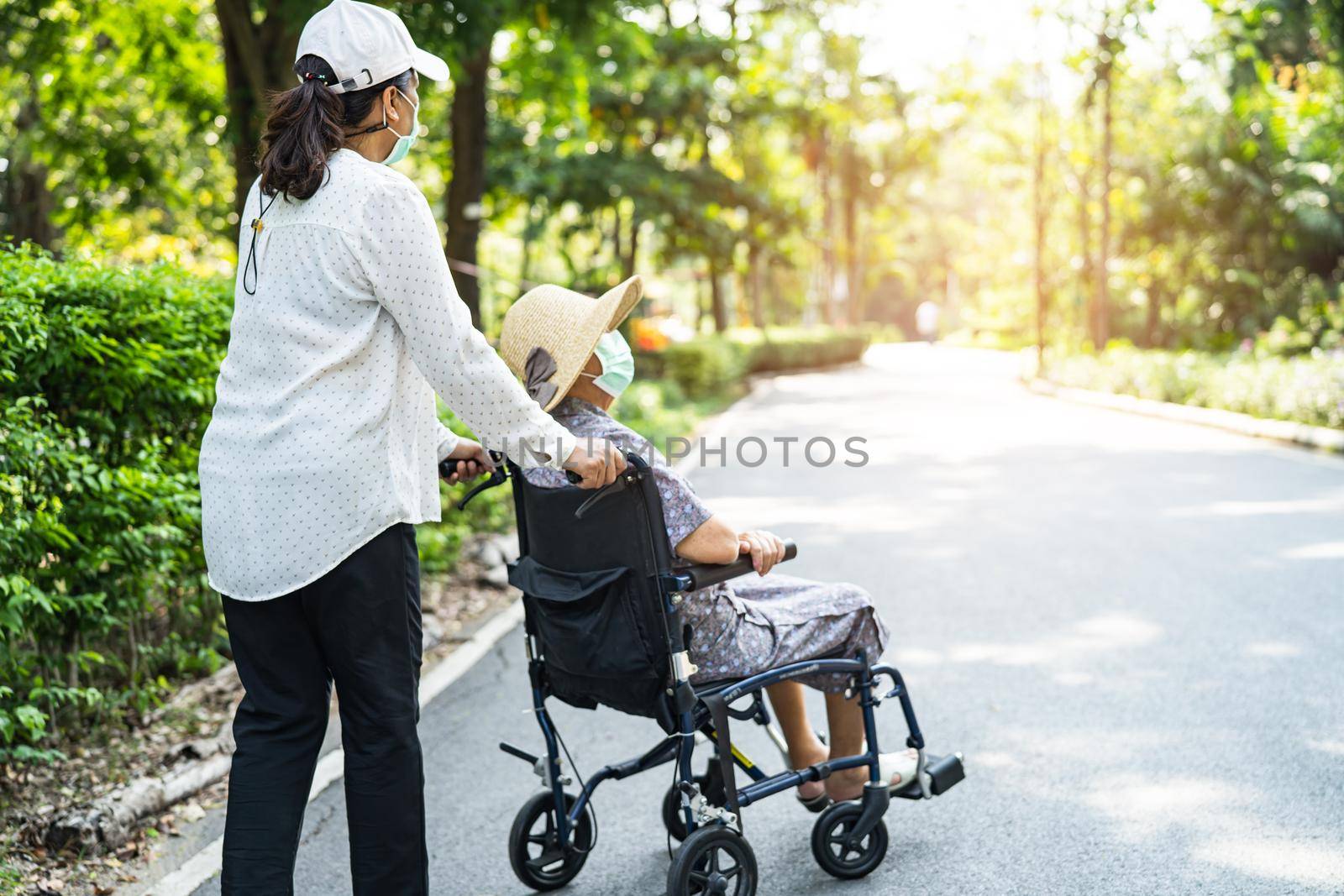Caregiver help and care Asian senior or elderly old lady woman patient sitting on wheelchair and wear a face mask to travel in park, by pamai