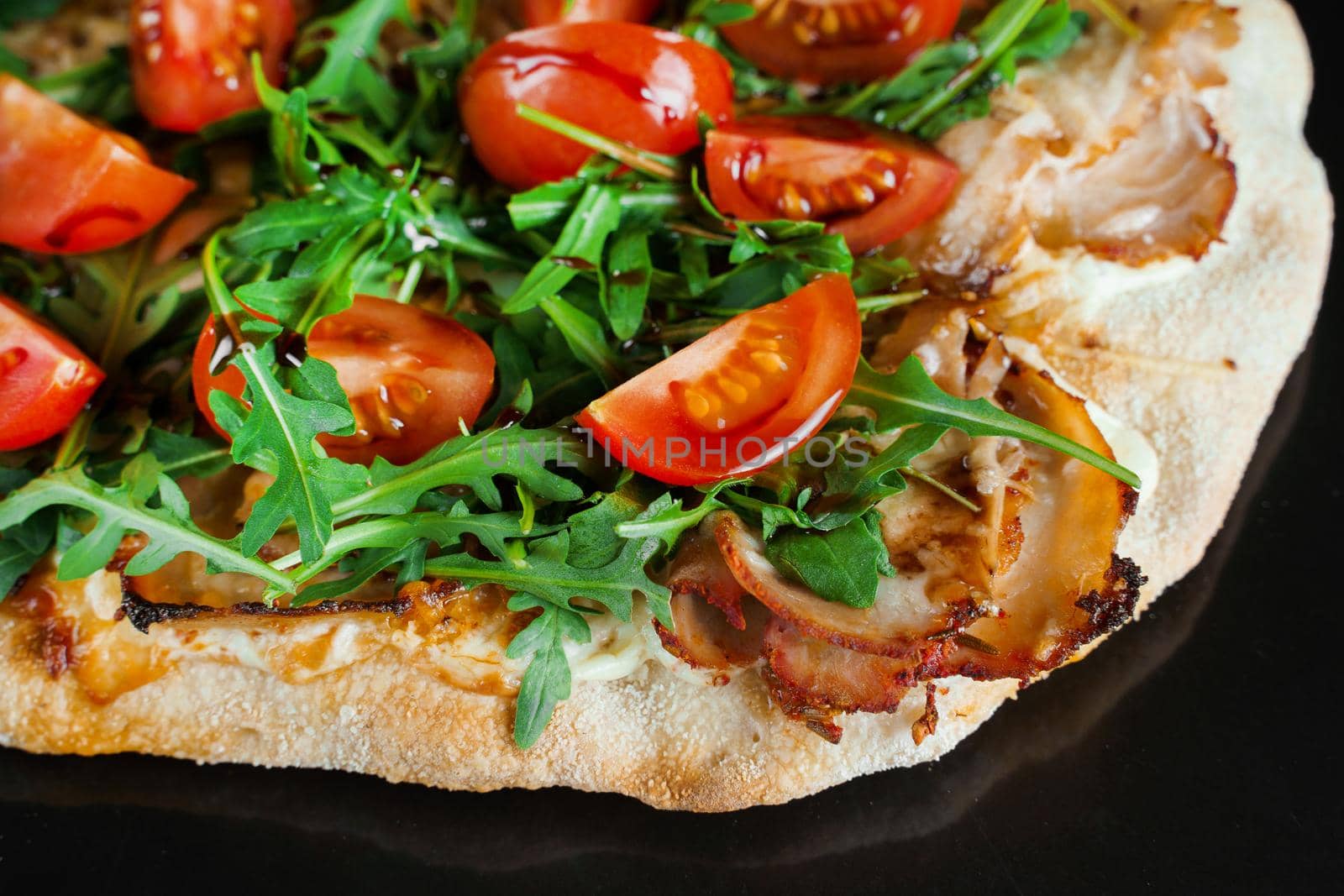 Pinsa romana gourmet italian cuisine on black background. Scrocchiarella. Pinsa with meat, arugula, tomatoes, cheese