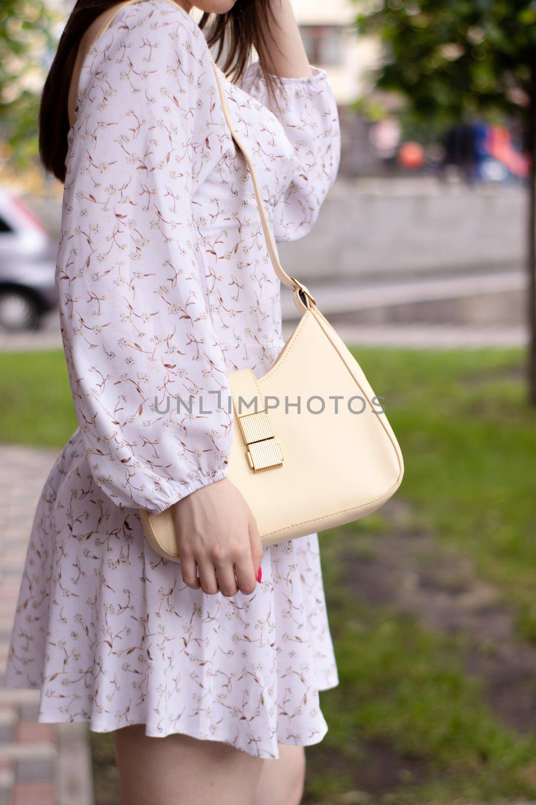 close up of woman in white dress holding fashionable beige purse outside. Product photography. stylish handbag for women by oliavesna