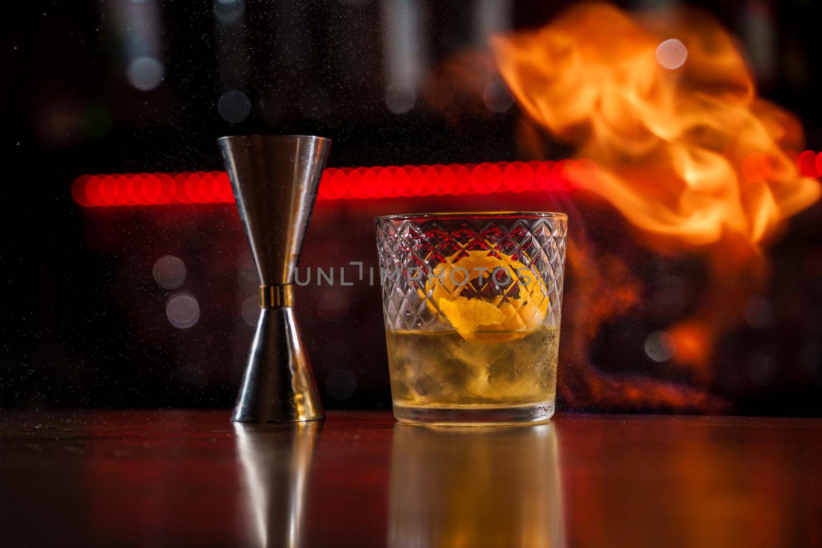 The bartender makes flame over a cocktail with orange peel close up.