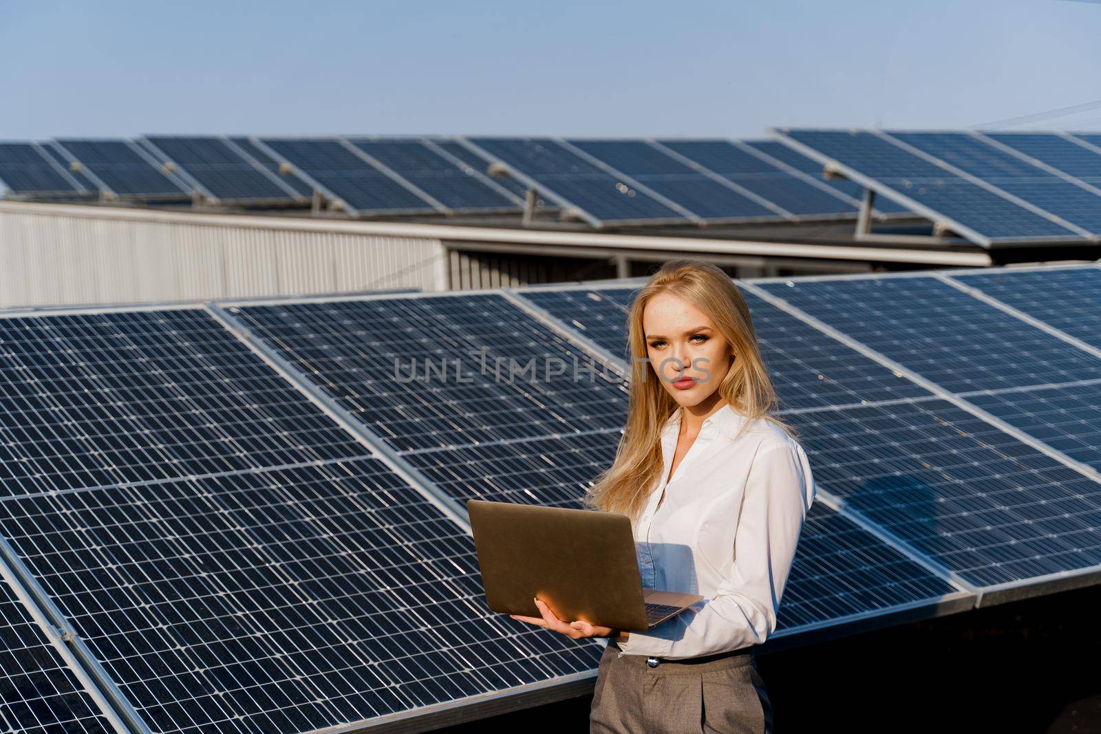 Investor woman stand with laptop near blue solar panels row on the ground. Free electricity for home. Sustainability of planet. Green energy by Rabizo