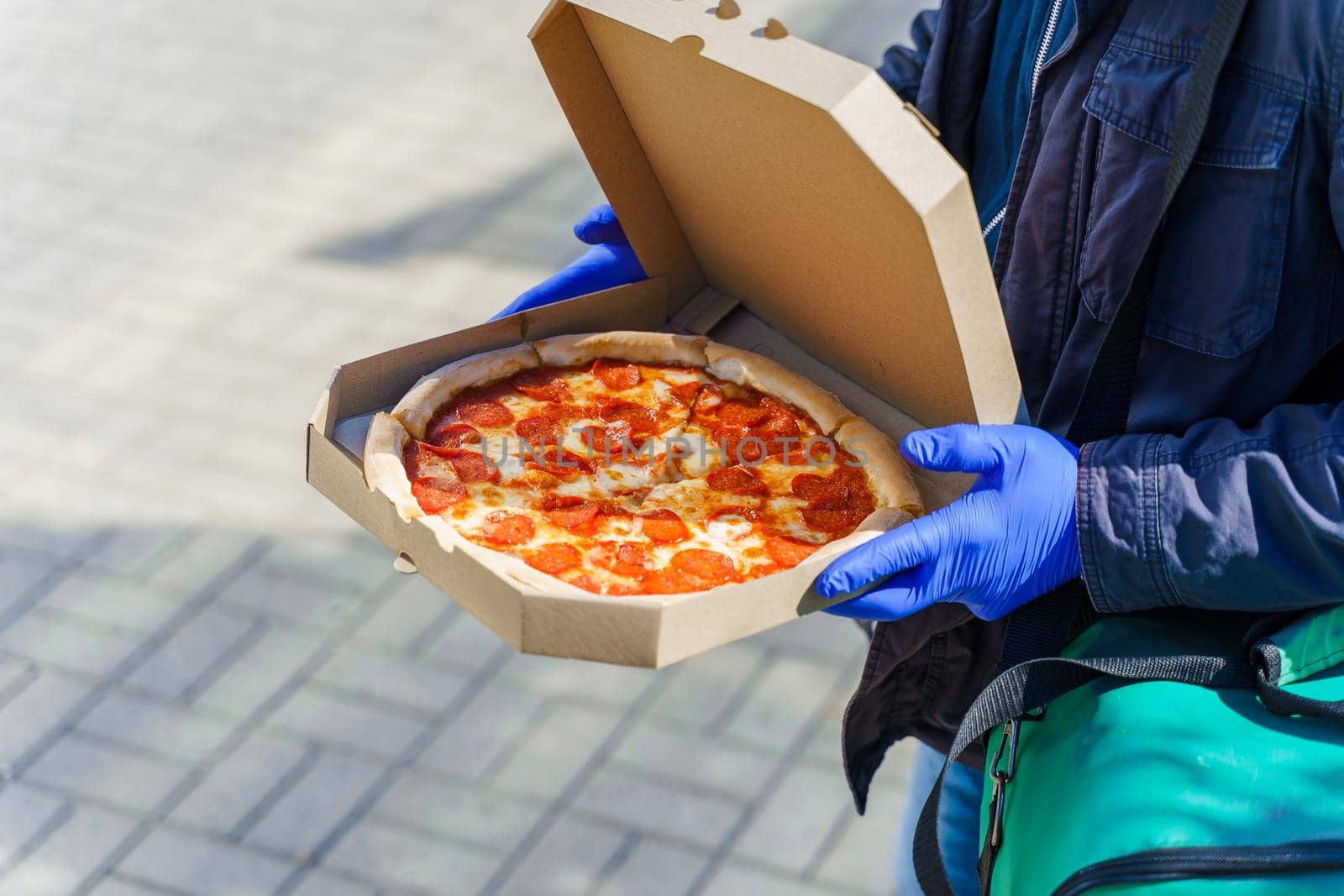 Pizza with salami and cheese in cardboard box. Safety delivery in blue medical gloves from restaurant. Quarantine for stop coronavirus covid-19. by Rabizo