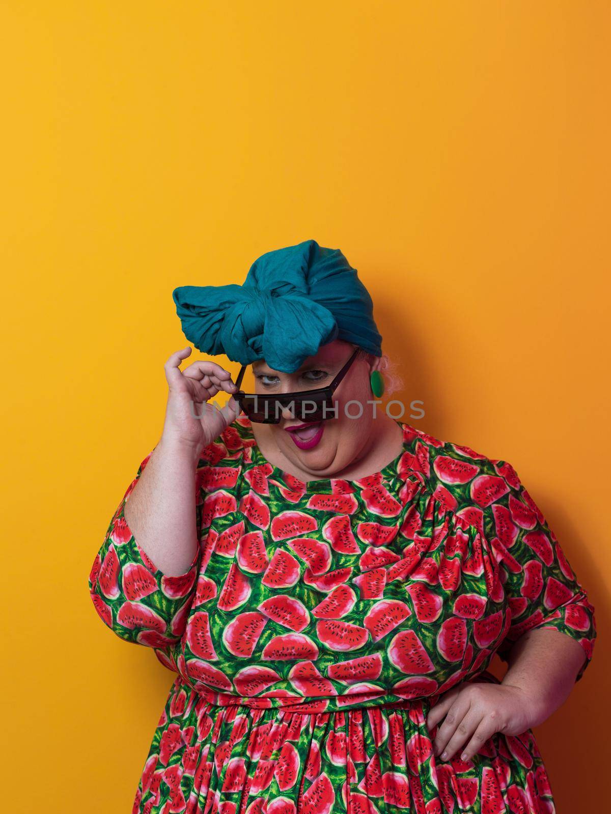 Funny plus size sexy model woman with trendy sunglasses, fashionable overweight blonde in colorful dress posing at the yellow fortuna gold background in studio. High quality photo