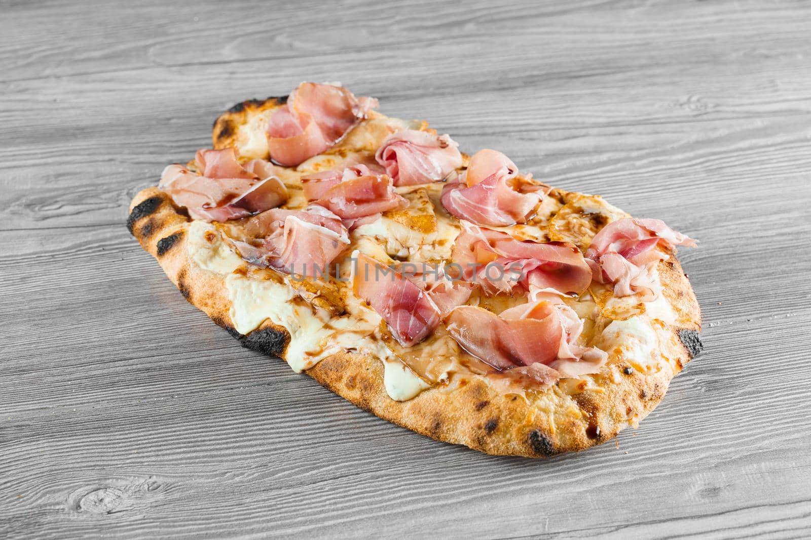 Scrocchiarella with pear, cheese, prosciutto on grey wooden background. Pinsa romana gourmet italian cuisine. Junk food by Rabizo