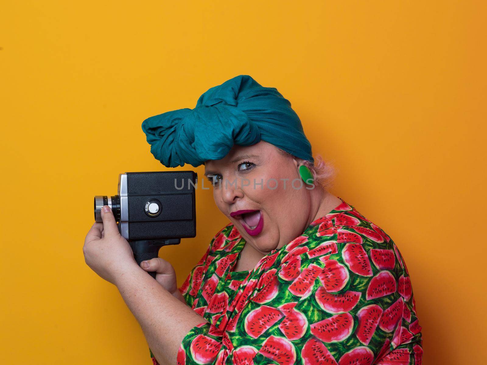 plus size smiling woman with funny emotional face expression with vintage camera in dress isolated on yellow background, traveler on vacation, summer fashion style, excited tourist. High quality photo