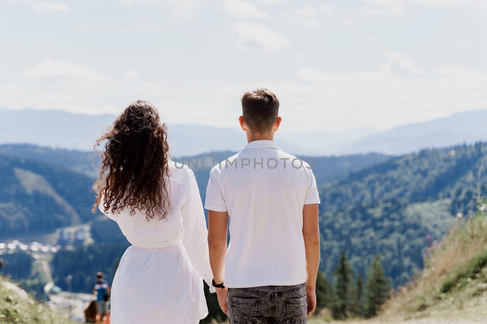 Couple is hugging and watching to the mountains. Life style of happy men and woman on the green hills. Advert for travelling agency. Tourism