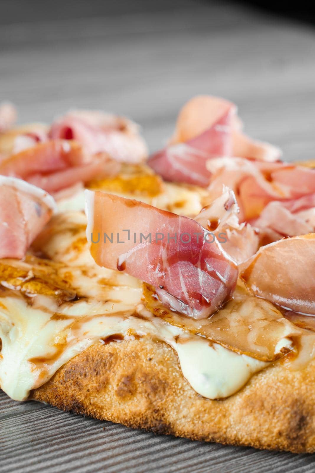 Scrocchiarella with pear, cheese, prosciutto on grey wooden background. Pinsa romana gourmet italian cuisine. Junk food.