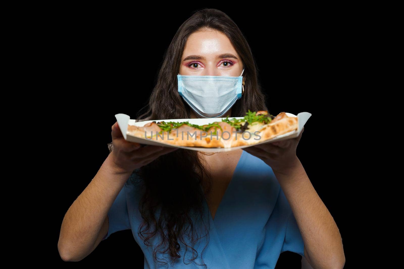 Girl courier with scrocchiarella gourmet italian cuisine on black background. Holding pinsa romana traditional dish. Food delivery from pizzeria. Pinsa with meat, arugula, olives, cheese by Rabizo