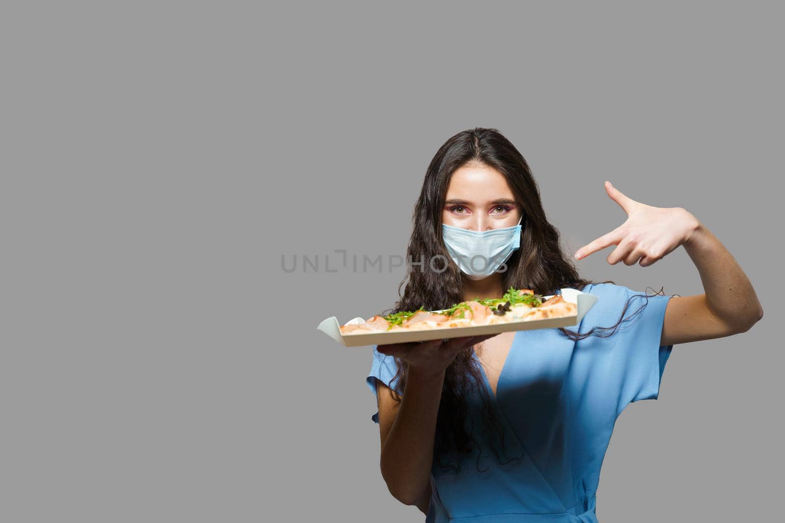 Girl courier with pinsa romana gourmet italian cuisine on grey background. Holding scrocchiarella traditional dish. Food delivery from pizzeria. Pinsa with meat, arugula, olives, cheese.