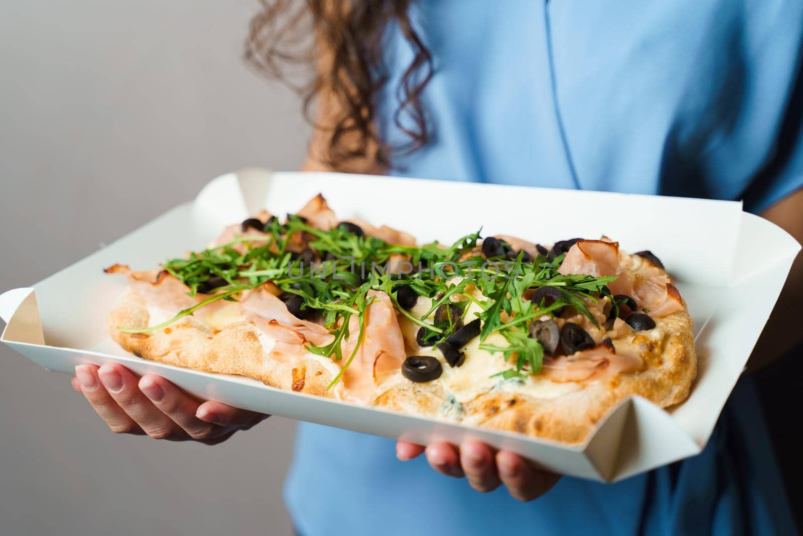 Pinsa romana in white delivery box. Courier holding crocchiarella gourmet italian cuisine on white background. Food delivery from pizzeria. Pinsa with meat, arugula, olives, cheese