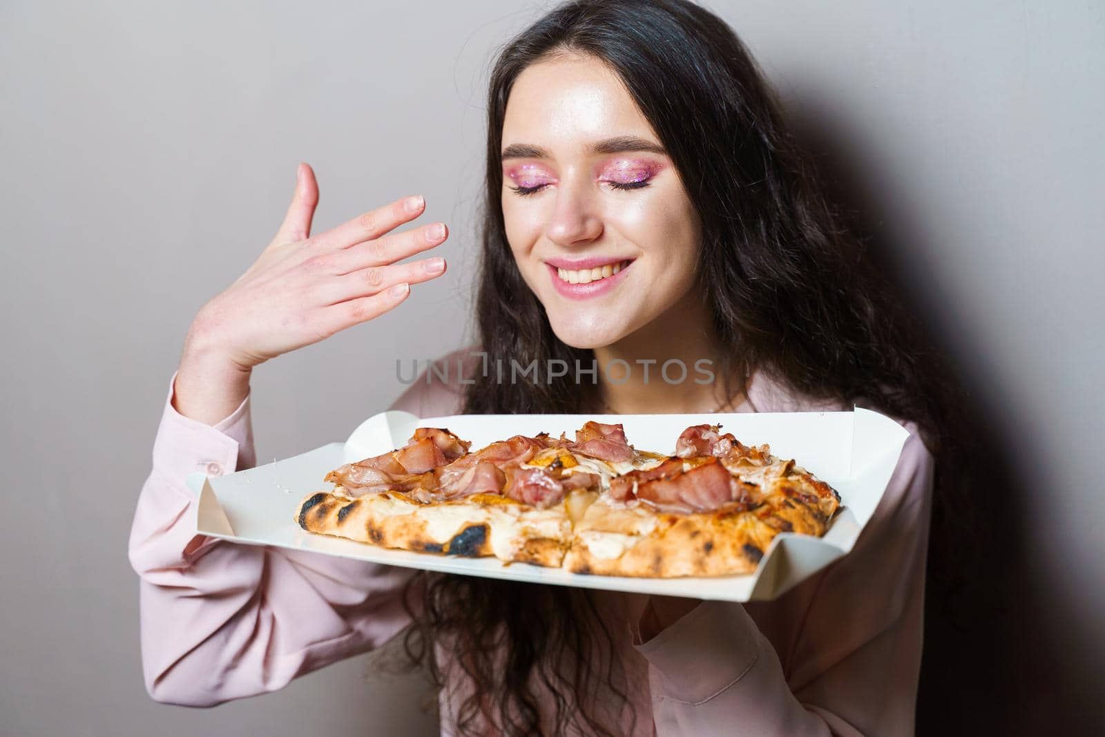 Girl courier with pinsa romana gourmet italian cuisine on grey background. Holding scrocchiarella traditional dish. Food delivery from pizzeria. Pinsa with meat, arugula, olives, cheese.