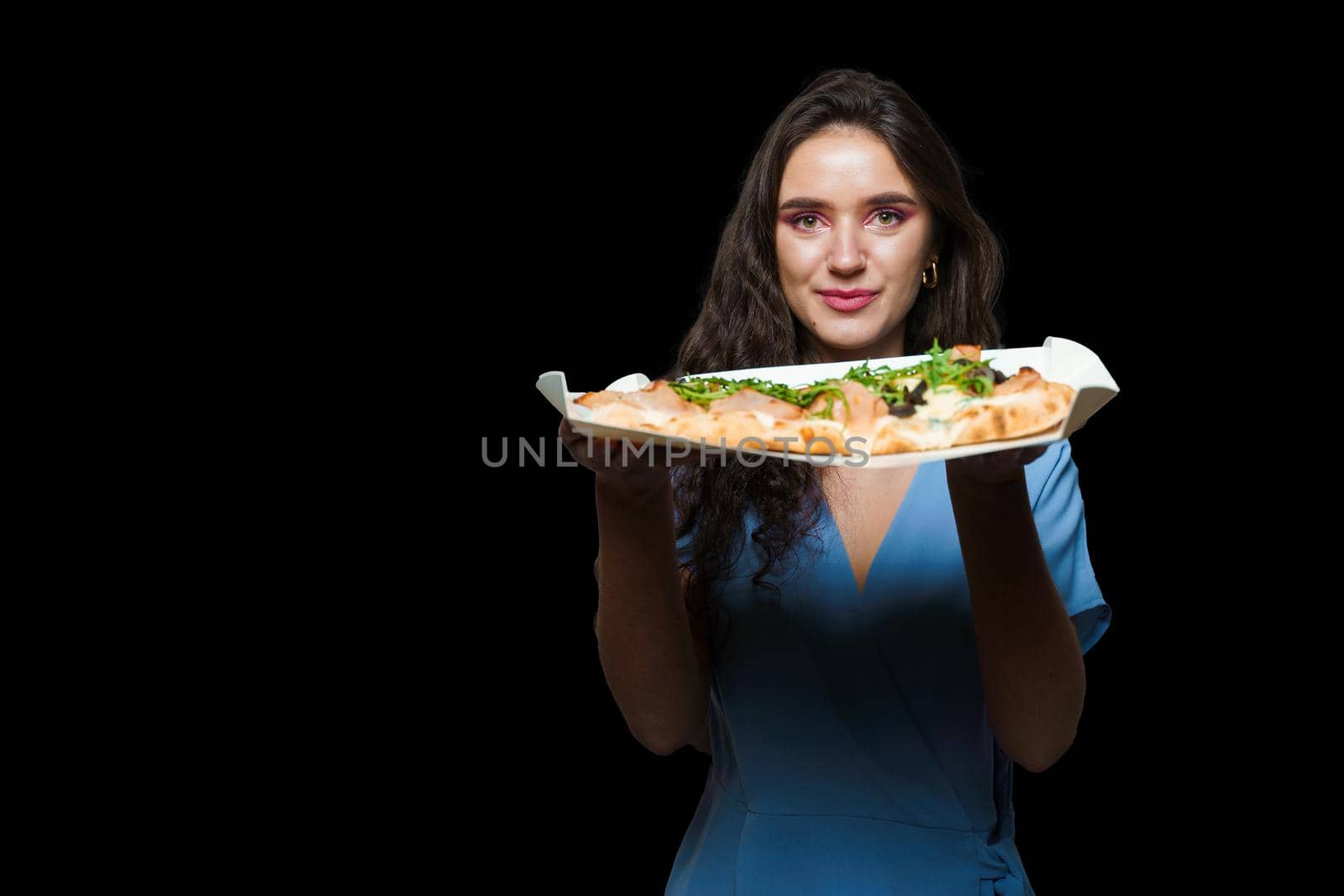 Woman courier with pinsa romana gourmet italian cuisine on black background. Holding scrocchiarella traditional dish. Food delivery from pizzeria. Pinsa with meat, arugula, olives, cheese