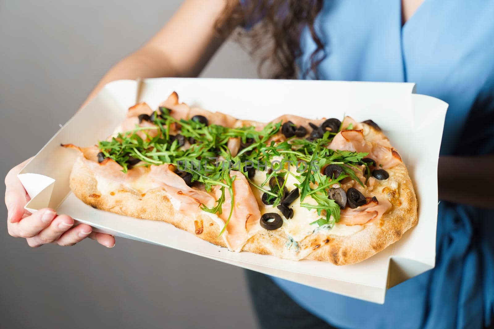 Pinsa romana in white delivery box. Courier holding crocchiarella gourmet italian cuisine on white background. Food delivery from pizzeria. Pinsa with meat, arugula, olives, cheese