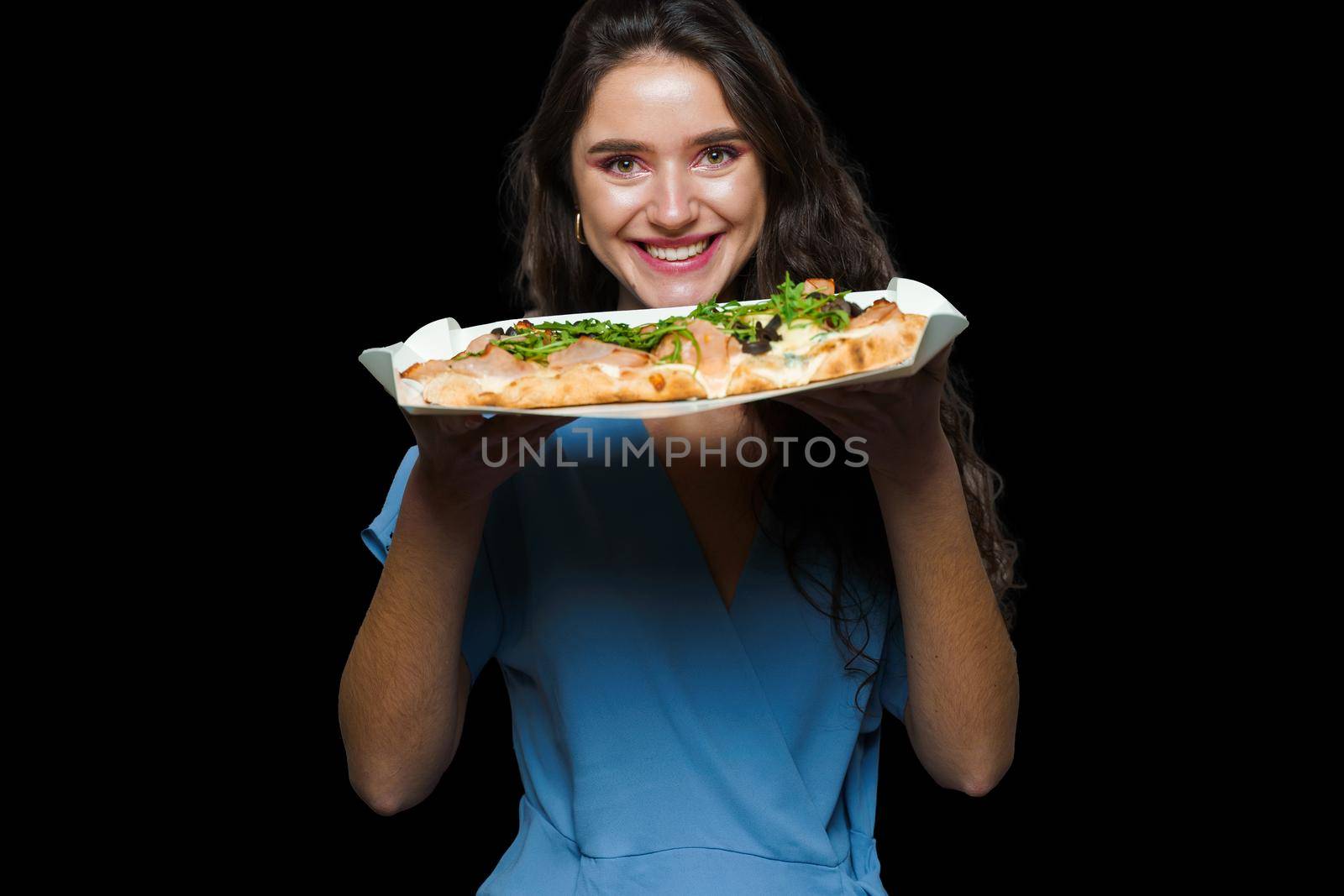 Woman courier with pinsa romana gourmet italian cuisine on black background. Holding scrocchiarella traditional dish. Food delivery from pizzeria. Pinsa with meat, arugula, olives, cheese