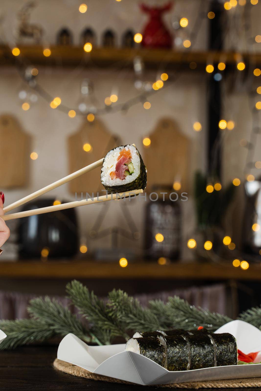 Holding sushi roll on the new year lights background. Christmas decoration. Food delivery at new year eve. Roll with salmon, tuna, cucumber and soft cheese