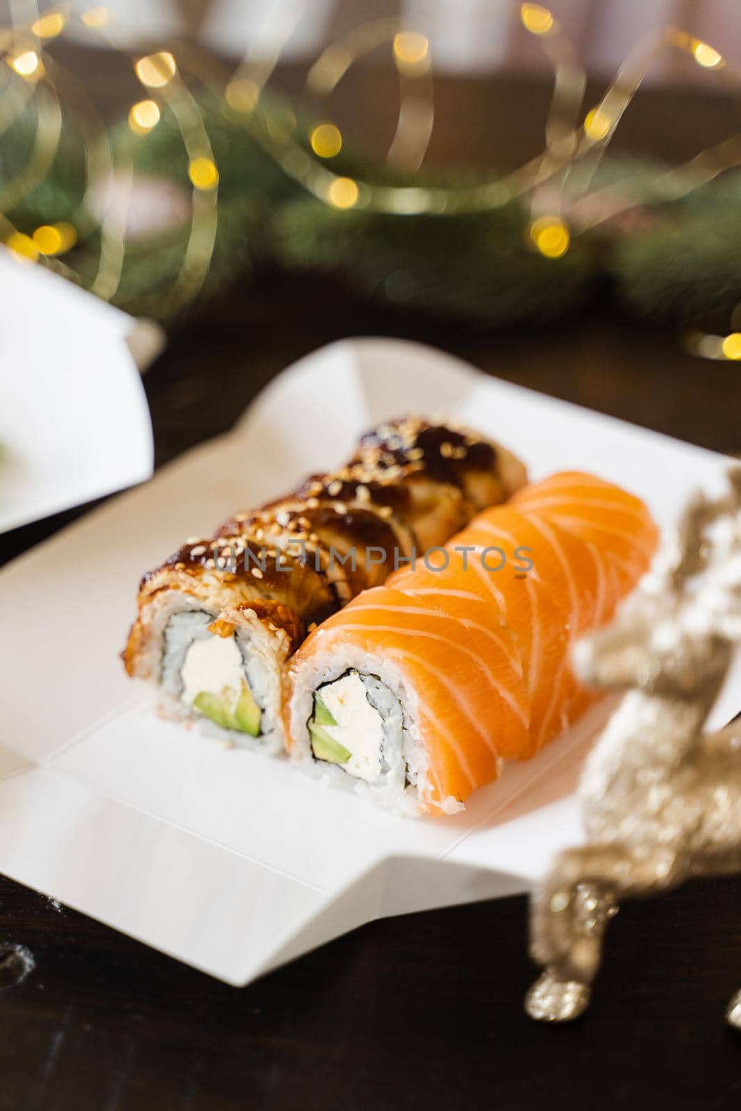 Sushi roll on the new year lights background. Christmas lights decoration. Food delivery at new year eve. Roll with salmon, eel, avocado and soft cheese