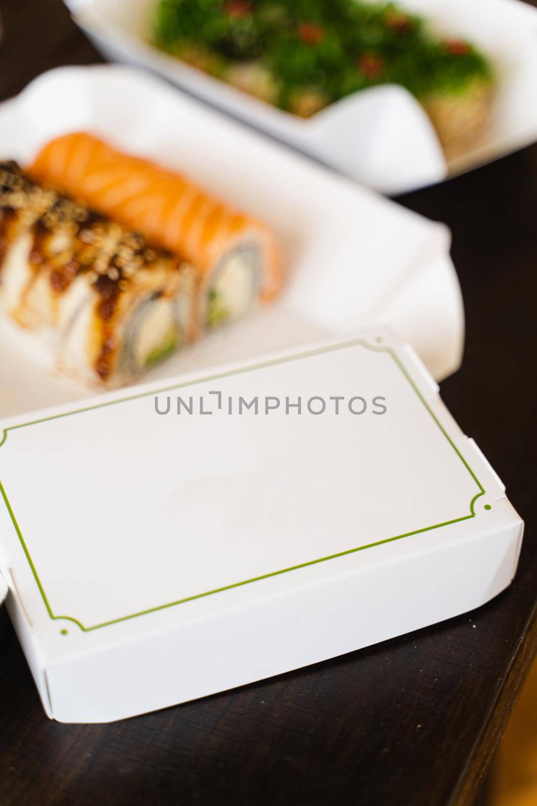 Cardboard box with blank place for logo of sushi delivery company. Sushi rolls on the background. by Rabizo
