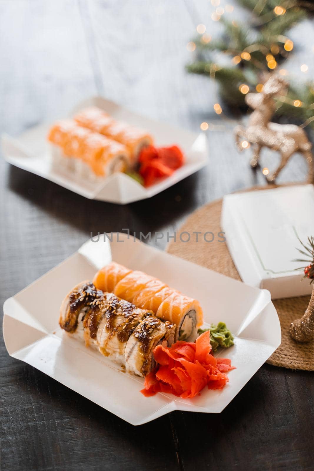 Sushi rolls on the new year lights background. Christmas decoration. Food delivery at new year eve. Roll with salmon, tuna, cucumber and soft cheese. by Rabizo