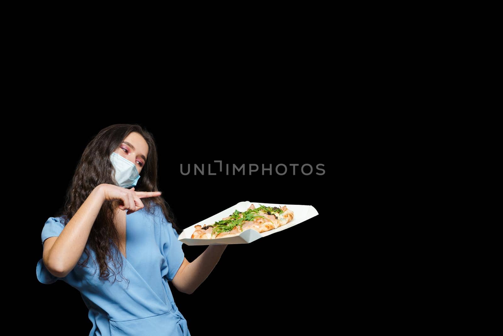 Girl courier with scrocchiarella gourmet italian cuisine on black background. Holding pinsa romana traditional dish. Food delivery from pizzeria. Pinsa with meat, arugula, olives, cheese.