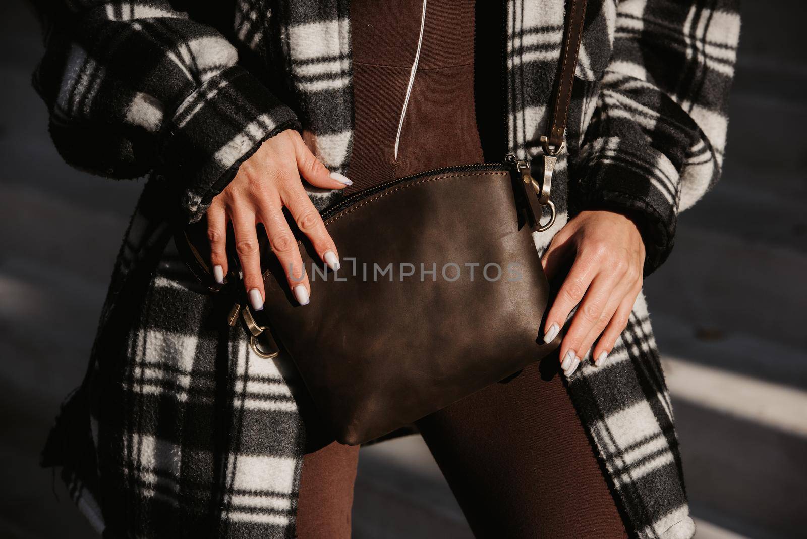 Outdoor fashion portrait of young fashionable girl wearing trendy checkered shirt, solid long sleeve bodycon one piece jumpsuits holding small brown color small bag.