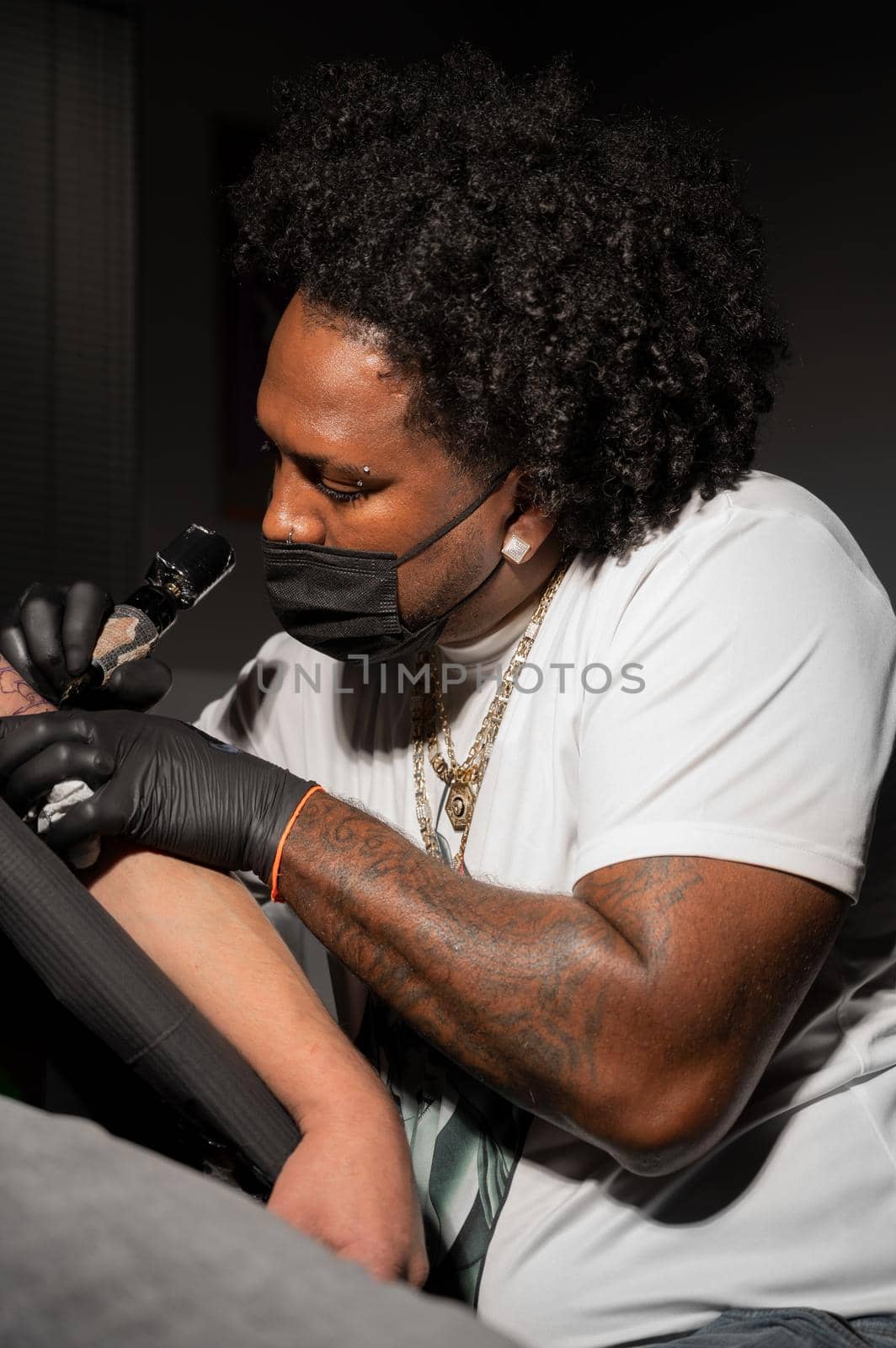 Professional African American tattoo artist makes a tattoo on client arm by HERRAEZ