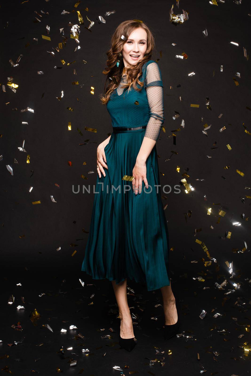 Front view of elegant woman wearing long black dress looking at camera and smiling on black isolated background. Attractive blonde with long legs posing in studio. Concept of party and beauty.