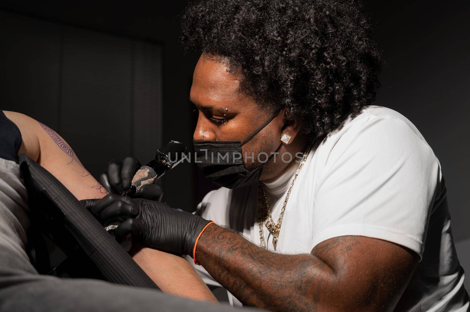 Professional African American tattoo artist makes a tattoo on client arm. High quality photography.