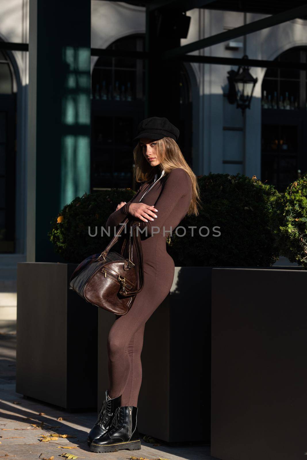 Fashionable young brunette woman with long legs wearing Solid Long Sleeve Bodycon One Piece Jumpsuits posing with a leather brown travel bag by Ashtray25