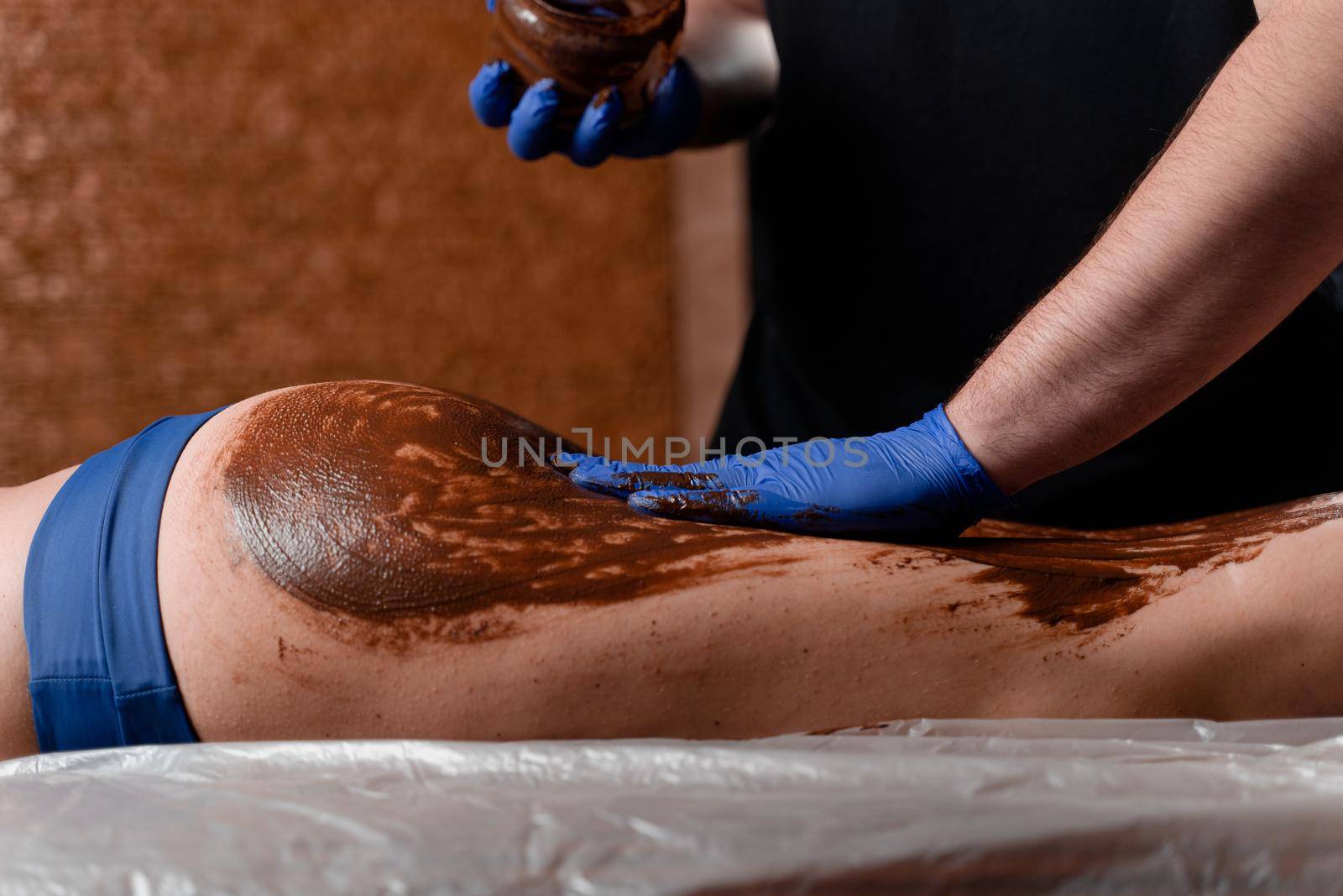 The masseur smears chocolate on the legs and thighs of the girl in the spa center. Beauty procedure chocolate wrap