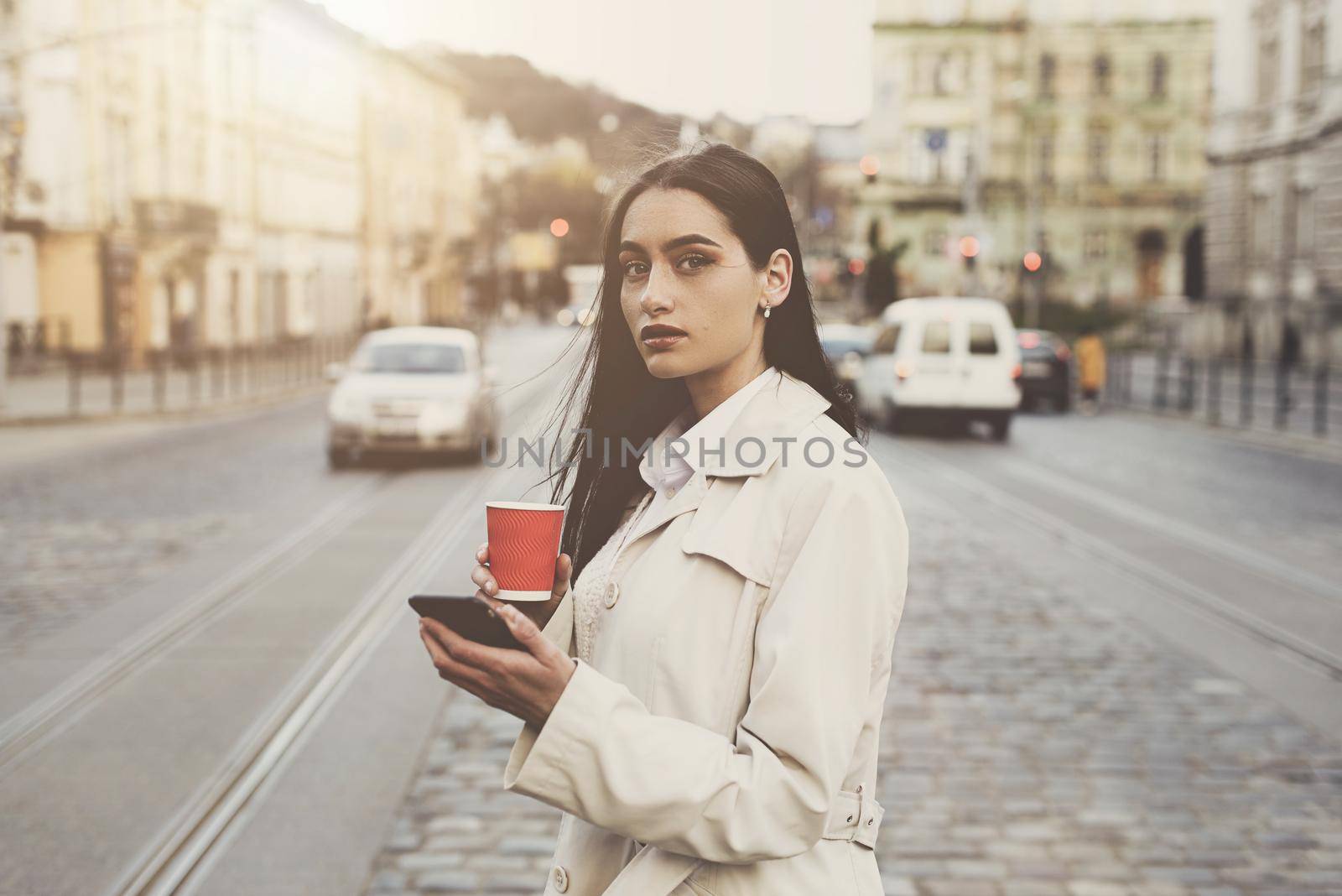 A woman on the street uses a mobile phone. online shopping. use of mobile applications. beautiful woman with long dark hair in a raincoat