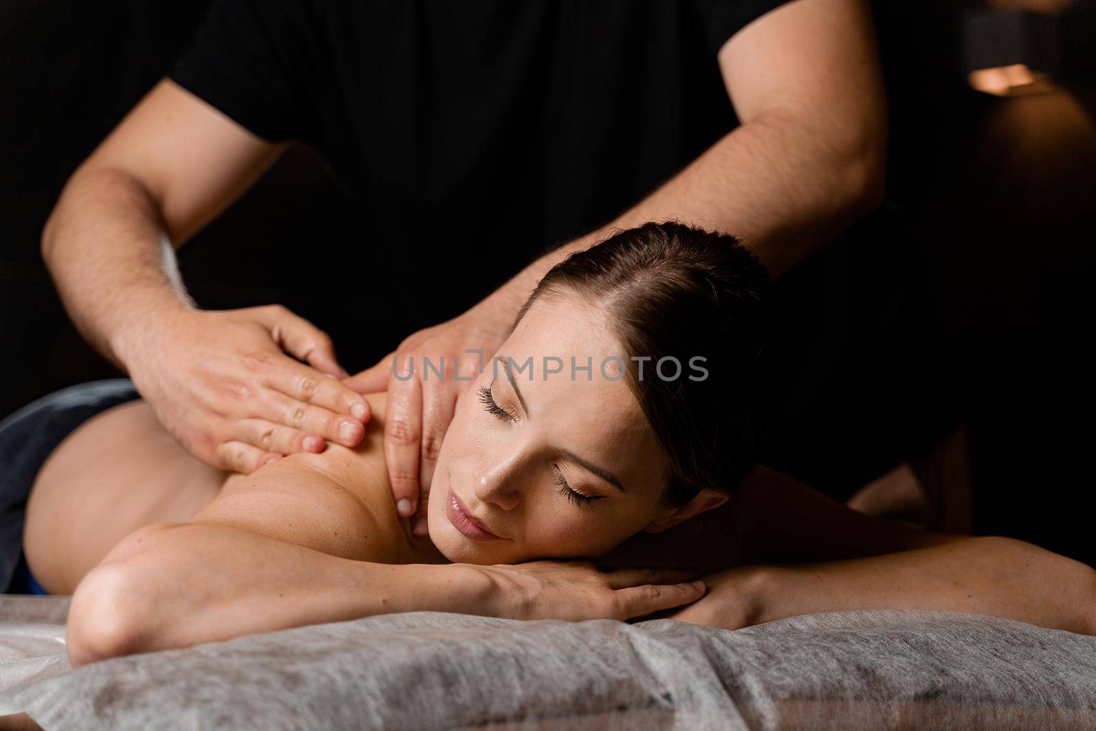 Attractive girl is relaxing on classic massage procedure in spa. Manual therapy. Masseur is doing shoulder massage