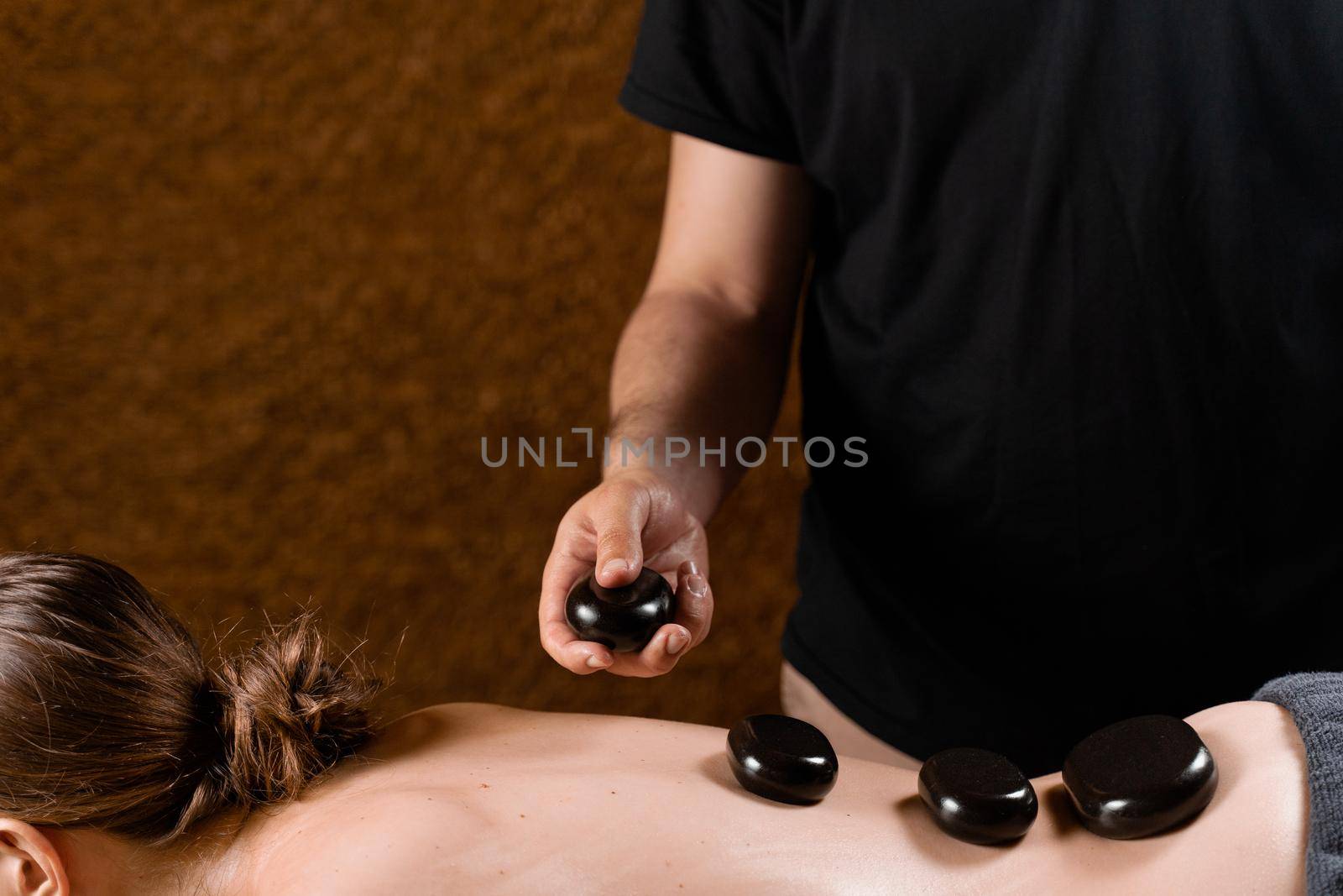 Heated stones on back of woman. Stone massage therapy in spa for relaxing. by Rabizo