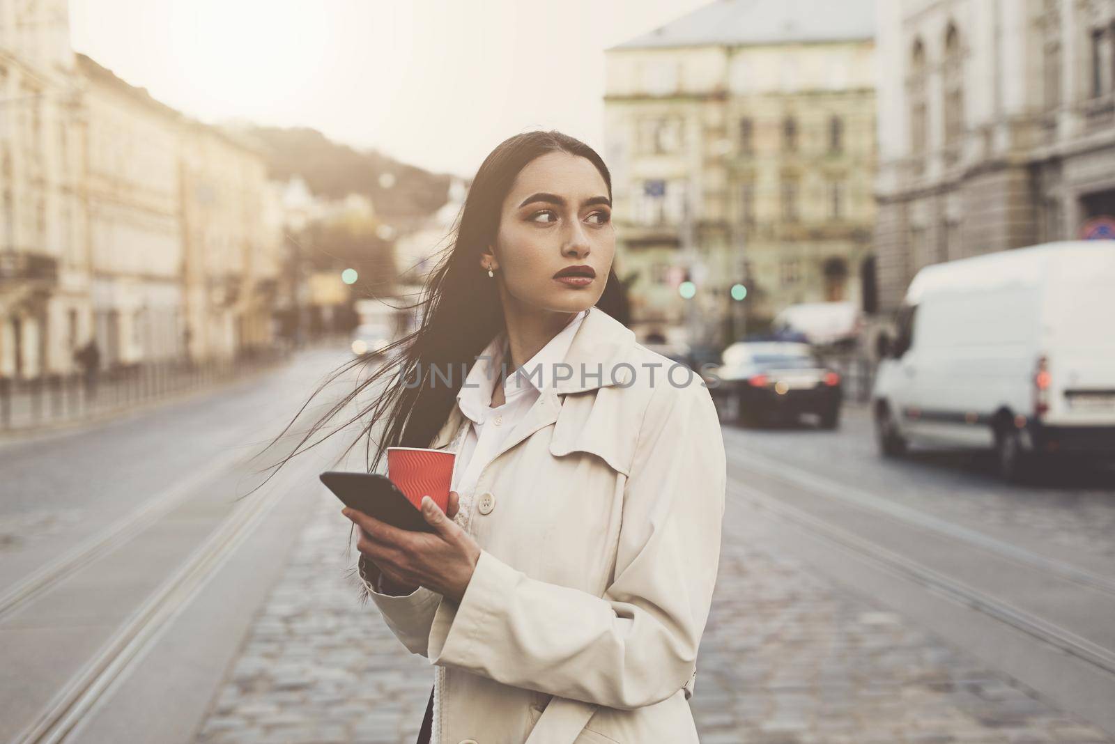 A woman on the street uses a mobile phone. online shopping. use of mobile applications. beautiful woman with long dark hair in a raincoat